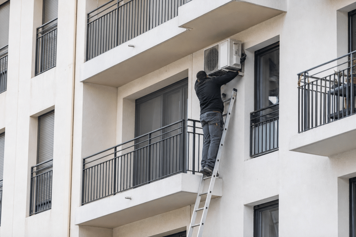 Technicien sur une échelle réparant un climatiseur de balcon