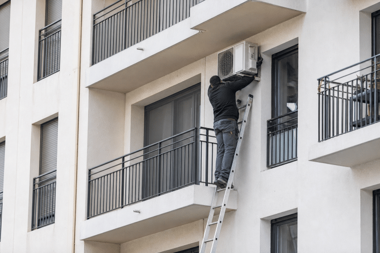 Technicien sur une échelle réparant un climatiseur de balcon